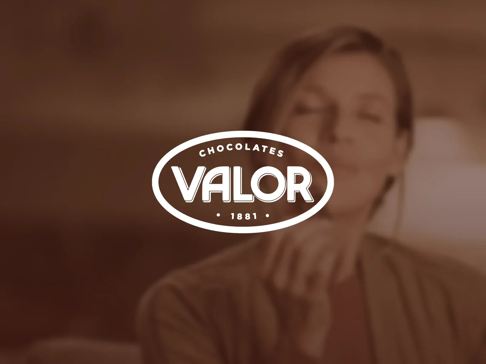 The Valor seal over a woman tasting a piece of chocolate, in chocolate brown